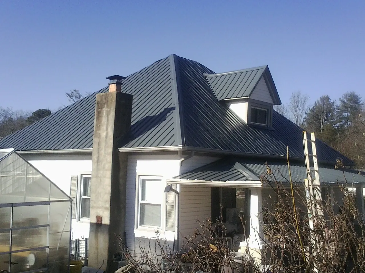 Dark blue standing seam metal roof on a white farmhouse with dormer — Slate & Tile Roof Repair by Roofing Brothers in Colorado Springs