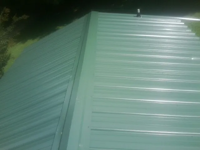 New green metal panels meeting at the ridge of a roof — Flat Roof Repair work by our crew in Colorado Springs
