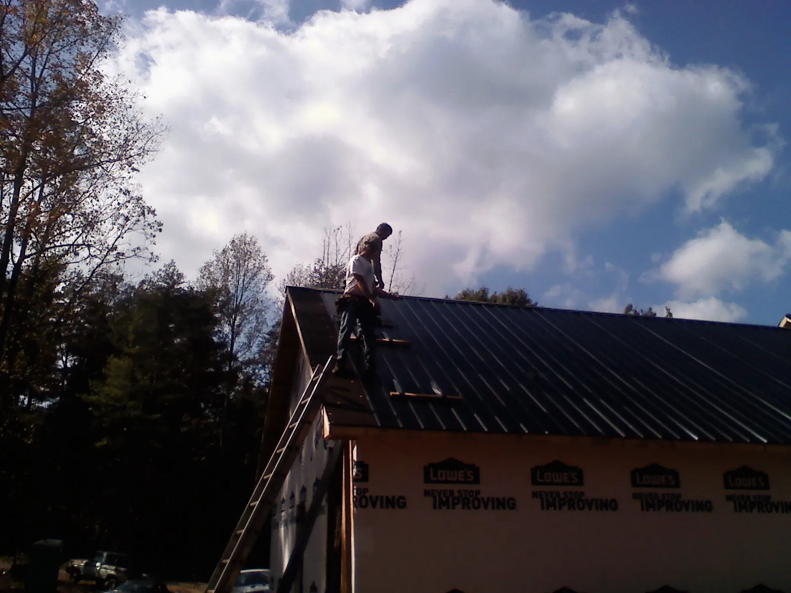 Roofer fastening dark metal panels high against a cloudy sky, from a Roof Inspection job in Colorado Springs
