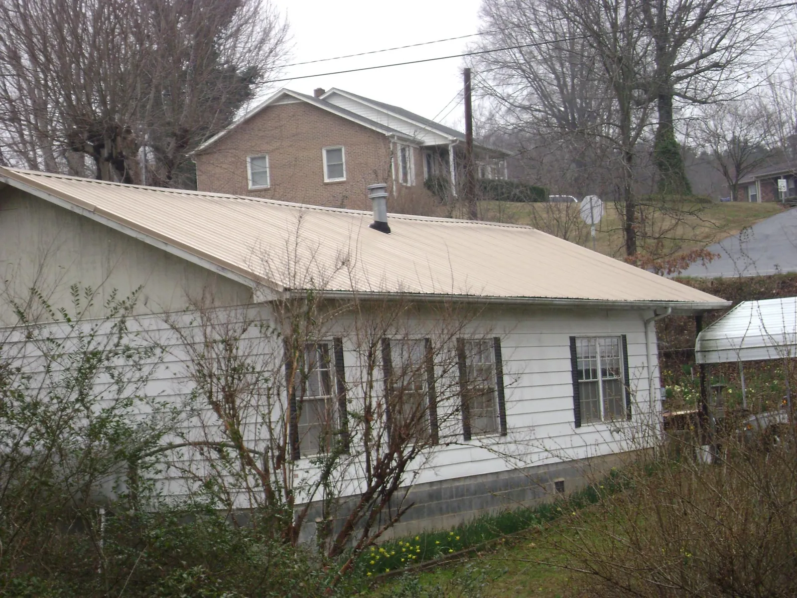 Tan metal roof on a white sided house set into a hillside — Commercial Roofing by Roofing Brothers in Colorado Springs